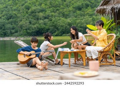 Young Asian man and woman enjoy outdoor lifestyle travel nature forest mountain on summer holiday vacation. Happy generation z people friends playing guitar and doing hobbies at lake house balcony. - Powered by Shutterstock