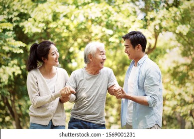 young asian man and woman helping senior man stand up and walk