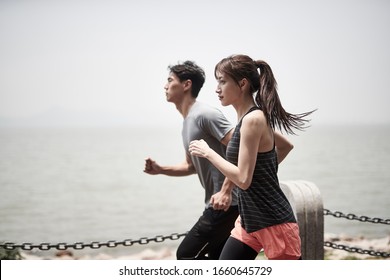 Young Asian Man And Woman Running Jogging Outdoors By The Sea, Side View