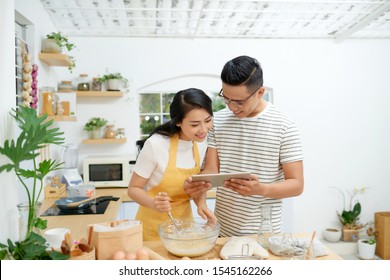 Young asian man and woman together cooking cake and bread with egg, looking menu from tablet in the flour happy relaxing in at home - Powered by Shutterstock