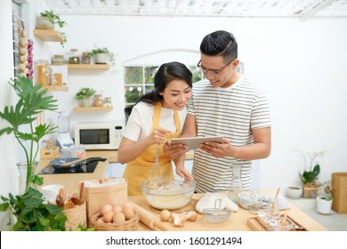 Young asian man and woman together cooking cake and bread with egg, looking menu from tablet in the flour happy relaxing in at home - Powered by Shutterstock