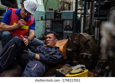 Young Asian man worker had a leg accident lying on the floor in metal lathe factory. Engineer supervisor talking on walkie talkie for help. Factory industrial safety and business insurance concept.