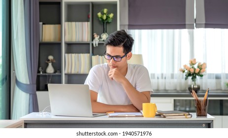 Young Asian Man Working At Home Using A Laptop Computer On A Table.