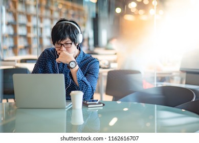 Young Asian Man Working With Laptop Computer On The Desk In Public Library. Male Student Doing Research In University College. Education And Learning Concepts