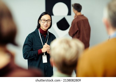 Young Asian man working in modern arts gallery standing in front of group of unrecognizable people speaking about exhibition - Shutterstock ID 2138082809