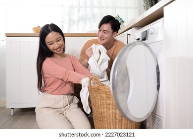 Young Asian married happy couple smiling and doing laundry at home. Boyfriend and girlfriend putting clothes in front loading washing machine together - Shutterstock ID 2227023121