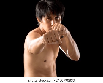 Young Asian Martial man in a fighting stance punching pose, focused and ready for training on black background - Powered by Shutterstock