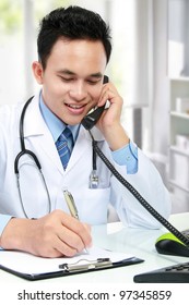 Young Asian Medical Doctor Writing A Note While Calling On The Phone