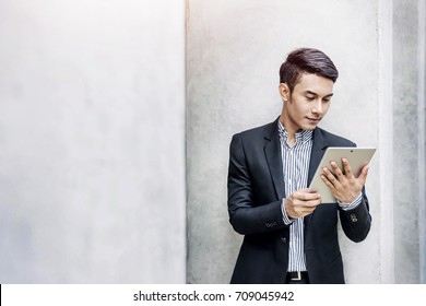 Young Asian And Modern Attractive Businessman Reading Or Working On A Digital Tablet Outside Office Building, Social Communicate Technology In Business Concept, Lifestyle Of Modern Male