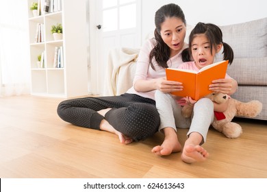 the young asian mom kept the story to the little girl before going to bed at noon children is scared of showing fear of expression and teddy bear sitting on wooden floor.