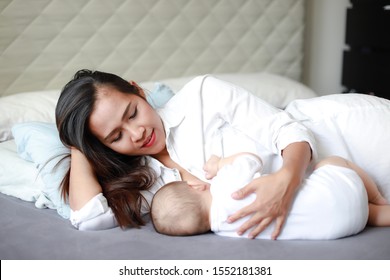 Young Asian Mother Breastfeeding Her Newborn Baby While Lying On Bed. Happy Healthy Mom And Son.