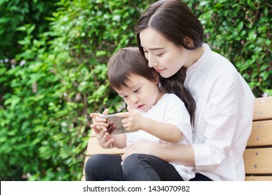 Young Asian Mother And Child Using Smart Phone In Park