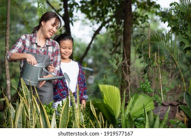 Young Asian Mother And Daughter Happy Working In The Garden Together On Weekend. Daughter Helping Mother Watering.