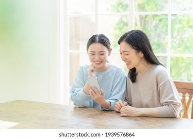 Young Asian Mother And Daughter Using Smart Phone In The Living Room