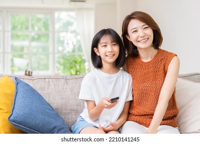 Young Asian Mother And Daughter Watching TV In Living Room