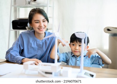 Young Asian Mother Is Energy Engineers Enjoy Spending Time With Little Kid Son Playing With Wind Turbine At Home Office, Teaching And Instilling Ideas About Natural Energy.