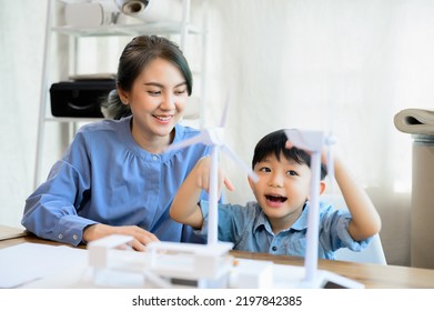 Young Asian Mother Is Energy Engineers Enjoy Looking At Her Son, Spending Time With Little Kid Son Playing With Wind Turbine At Home Office, Teaching And Instilling Ideas About Natural Energy.