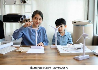 Young Asian Mother Is An Energy And Environmental Engineer Spending Time With Little Kid Son At Home Office, Teaching And Instilling Ideas About Natural Energy With Wind Turbine Model. Focus Turbine.