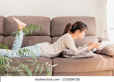 Young asian mother enjoying her time alone lying on the sofa watching the news on a tablet. Girl comfortable relaxing at home on the couch using tablet.