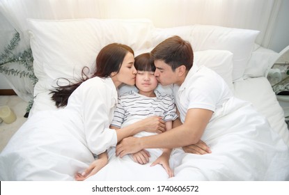 Young Asian Mother, Father And Boy Sleeping In Bed, Mom And Dad Kiss On Cheek Of Son,view From Above