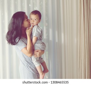 Young Asian Mother Is Kissing Her Lovely One Year Old Son.Vintage Photo. Mom And Baby Son Family Concept Idea.