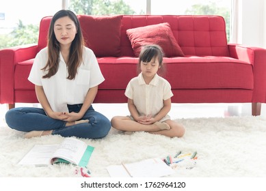 Young Asian Mother And Little Child Daughter Doing Meditation Sit On The Floor At Home, Mom Teaching Cute Kid Girl Learning Practice Meditation Together, Family Joyful Together In A House On Holiday

