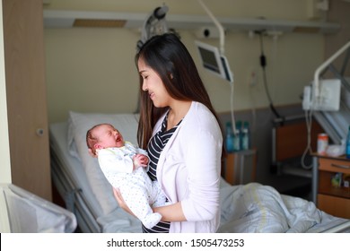 Young Asian Mother Looking To Little Infant Newborn Baby In Her Arms And Smiling In Delivery Room At Hospital After Giving Birth.