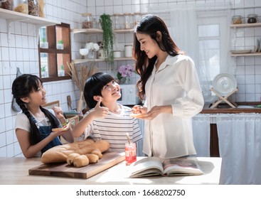 Young Asian Mother With Son Child And Daughter Eat Yam With Bread In Kitchen, Happy Family Have Leisure Time In Home.