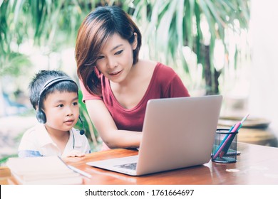 Young Asian Mother And Son Using Laptop Computer For Study And Learning Together At Home, Boy Wearing Headphone For E-learning With Distancing, Teacher Or Mom Support Child, Education Concept.