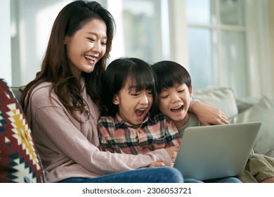 young asian mother and two children sitting on family couch at home using laptop computer together - Powered by Shutterstock