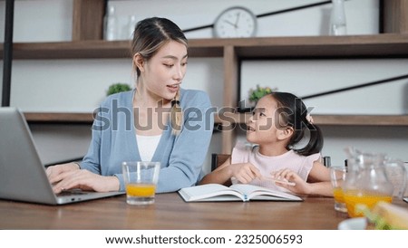 Young asian mother working on laptop while little daughter doing homework at home. Working and education concept, Single mother concept