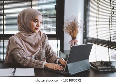 Young Asian Muslim Business Woman Brown Hijab Sitting And Working With Laptop Computer At Modern Office.