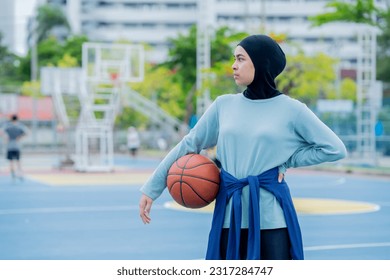 Young asian muslim girl teen wearing hijab going to play basketball on the outdoor court in the morning with determination, Muslim sport concept. - Powered by Shutterstock