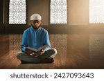 Young asian muslim man with beard reading holy book quran in the mosque window arch