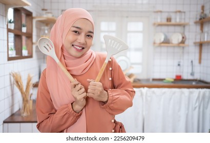 Young Asian Muslim woman housewife wearing Hijab cooking and holding pan and spatula on kitchen background. - Powered by Shutterstock