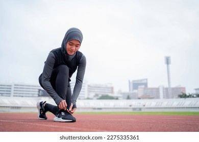 A young asian Muslim woman wearing a black hijab is exercising and running at an outdoor stadium in the morning. Modern Muslim woman concept,  Muslim woman sport concept, Islam - Powered by Shutterstock