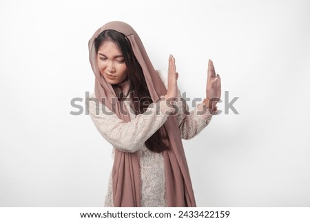 Young Asian Muslim woman wearing veil hijab gesturing a no rejection, refuse using hands and fingers, isolated by white background. Ramadan and Eid Mubarak concept