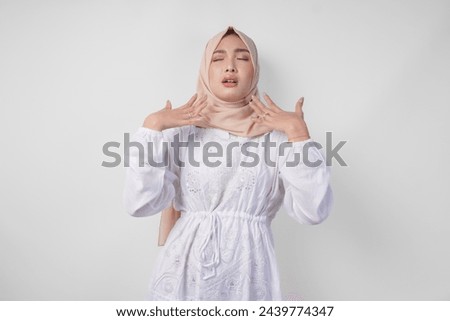 Young Asian Muslim woman in white dress and hijab raising hand to fan herself feeling hot due to summer weather while fasting. Ramadan concept [[stock_photo]] © 