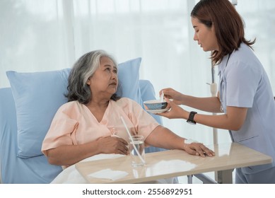 Young Asian nurse feeding breakfast to senior woman patient on bed in hospital ward, elderly care concept - Powered by Shutterstock