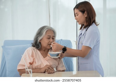 Young Asian nurse feeding breakfast to senior woman patient on bed in hospital ward, elderly care concept - Powered by Shutterstock