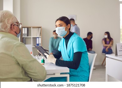 Young Asian Nurse Informs An Older Man About The Benefits And Possible Side Effects Of The Vaccine. Doctor Talks To The Old Person Before Giving The Injection During The Vaccination Period.