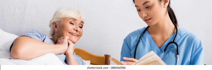 Young Asian Nurse Reading Book To Happy Aged Woman In Hospital, Banner