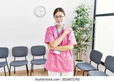 Young Asian Nurse Woman At Medical Waiting Room Pointing With Hand Finger To The Side Showing Advertisement, Serious And Calm Face 