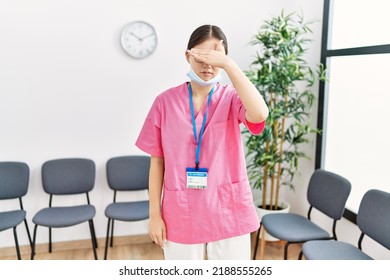 Young Asian Nurse Woman At Medical Waiting Room Covering Eyes With Hand, Looking Serious And Sad. Sightless, Hiding And Rejection Concept 