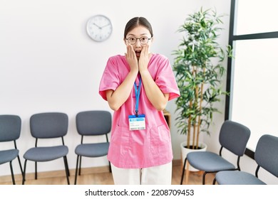 Young Asian Nurse Woman At Medical Waiting Room Afraid And Shocked, Surprise And Amazed Expression With Hands On Face 