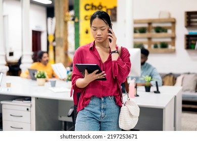 Young Asian Office Worker Standing In The Office Holding A Digital Tablet And Talking On The Phone.