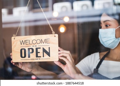 Young asian owner retail,coffee shop woman turning sign board to open with wearing face mask,protection to pandemic of coronavirus.Close, closed store,restaurant due to lockdown, quarantine of covid.