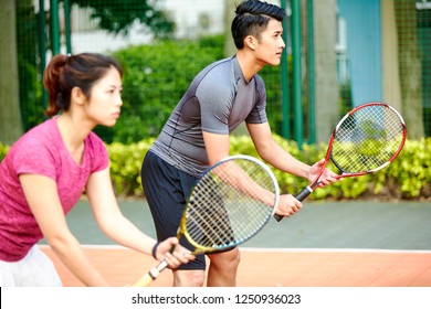young asian pair of man and woman tennis players in a mixed double match, focus on the background man