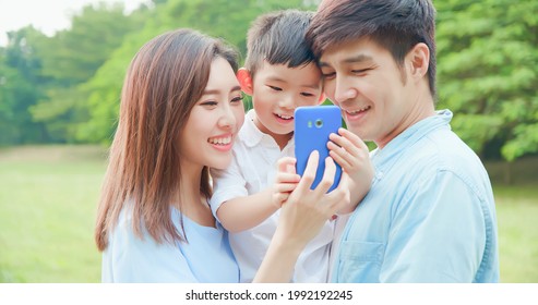 Young Asian Parent And Kid Look Smartphone Happily At Park