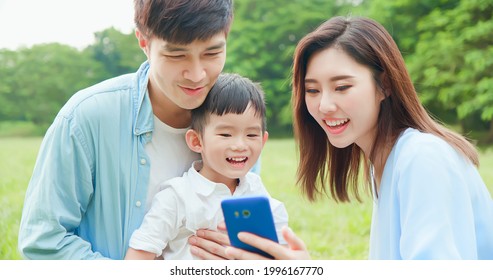 Young Asian Parent And Kid Look Smartphone Happily At Park